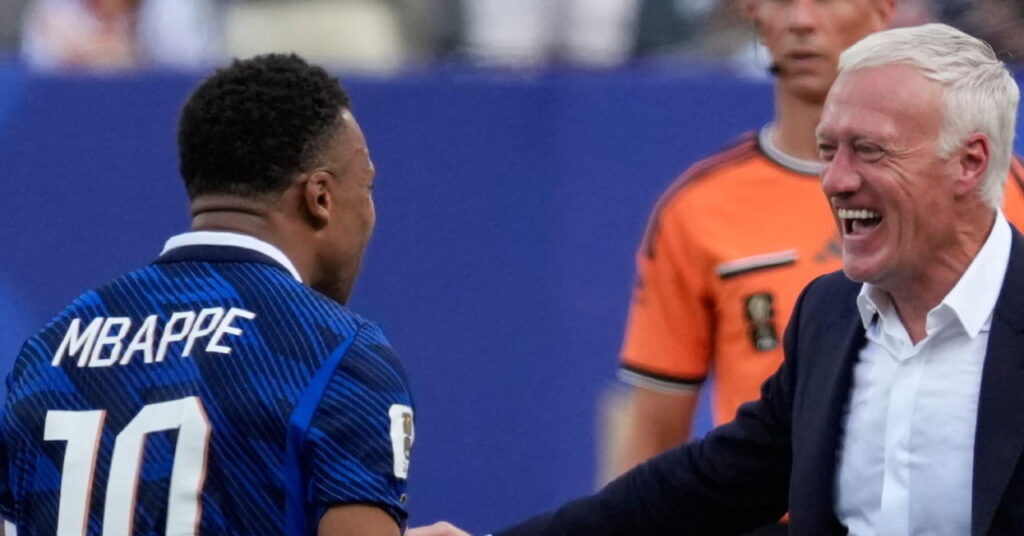 Le footballeur Kylian Mbappe regarde à sa droite et célèbre sur un terrain tout en portant un maillot bleu de l'équipe de France de football avec son nom et son numéro 10 dans le dos lors de la Coupe du monde 2026, célébrant avec l'entraîneur-chef Didier Deschamps, qui sourit et porte une veste de costume sombre et une chemise blanche