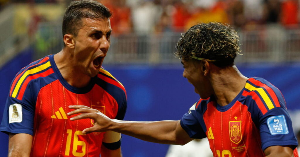 Les footballeurs espagnols Rodri, qui rugit, et Lamine Yamal, qui lève la main droite et sourit, célébrant un but sur un terrain de football lors de la Coupe du Monde de football de la FIFA 2026, portant le maillot rouge de l'équipe nationale avec du jaune et du bleu.