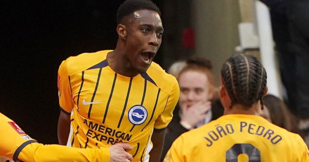 Le footballeur Danny Welbeck sautant et criant pour célébrer un but alors qu'il jouait pour le Brighton and Hove Albion Football Club dans un kit jaune avec des rayures bleu foncé et ses coéquipiers le félicitant
