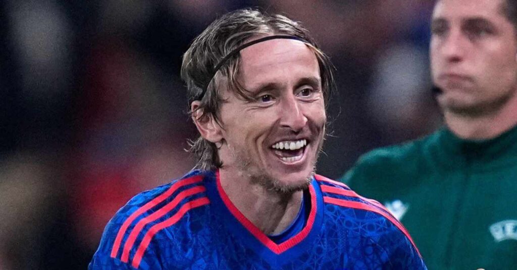 Le footballeur de l'AC Milan, Luka Modric, sourit pour célébrer un but alors qu'il jouait pour l'équipe nationale de football de Croatie dans une chemise bleue avec une bordure Adidas rouge sur les épaules et le cou.