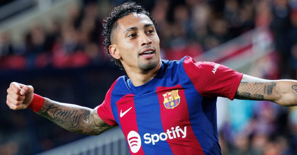 Le footballeur brésilien Raphinha utilise son bras gauche levé pour célébrer un but de l'équipe de la Liga Barcelona Football Club dans un haut bleu foncé et rouge