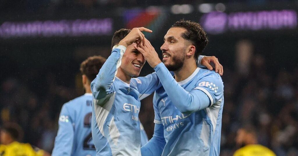 Le footballeur Phil Foden lève le bras gauche et place sa gauche par-dessus l'épaule de son coéquipier Rayan Cherki tandis que les joueurs sourient pour célébrer un but de l'équipe de Premier League du Manchester City Football Club. Les deux hommes portent des chemises bleu clair avec des détails blancs et les mots logos Etihad Airways et Puma visibles sur la poitrine.