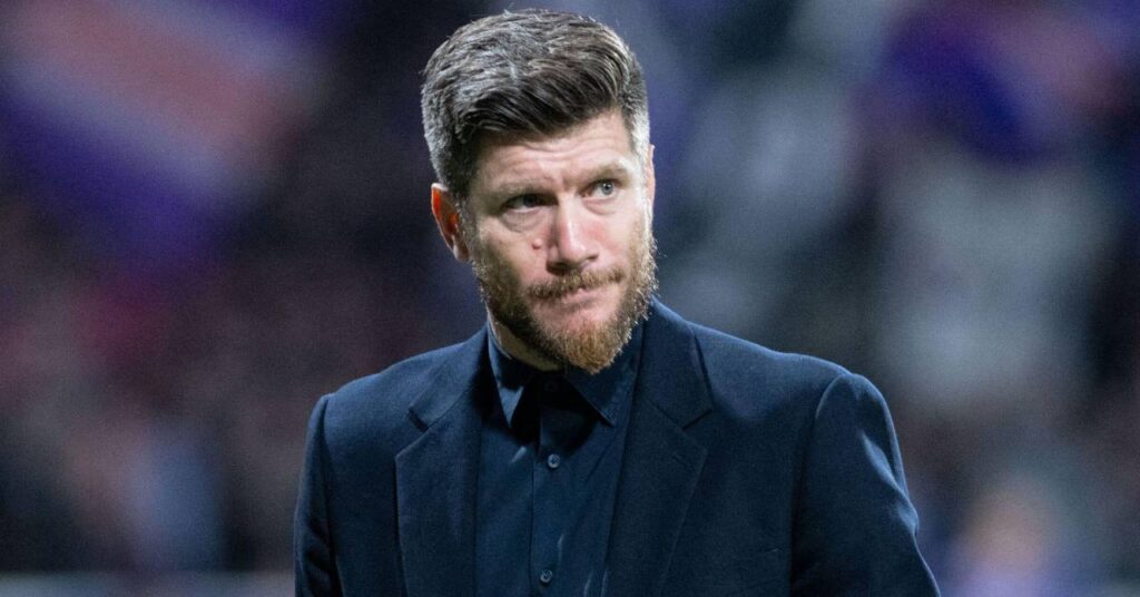 Sébastien Pocognoli, entraîneur de football et entraîneur de l'équipe nationale d'Écosse, regarde à sa gauche sur un terrain dans un stade tout en portant une veste et une chemise de costume sombre